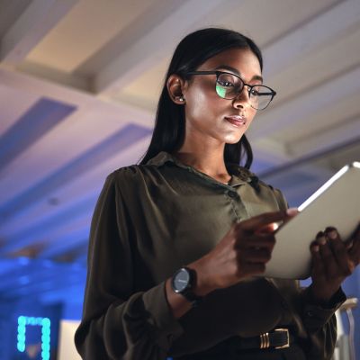 Tablet, designer and serious woman research in business startup office at night on deadline. Technology, creative professional or Indian entrepreneur reading information, email or app in neon company